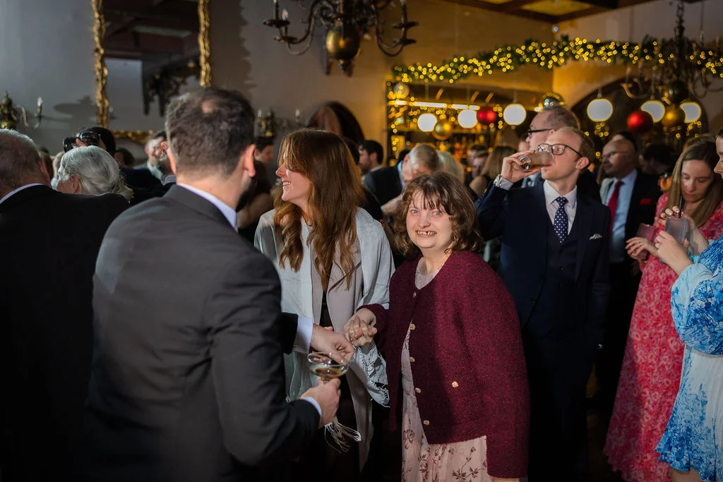 Wedding guests mingle and enjoy drinks in a warm, festoon-lit reception venue during a winter celebration.
