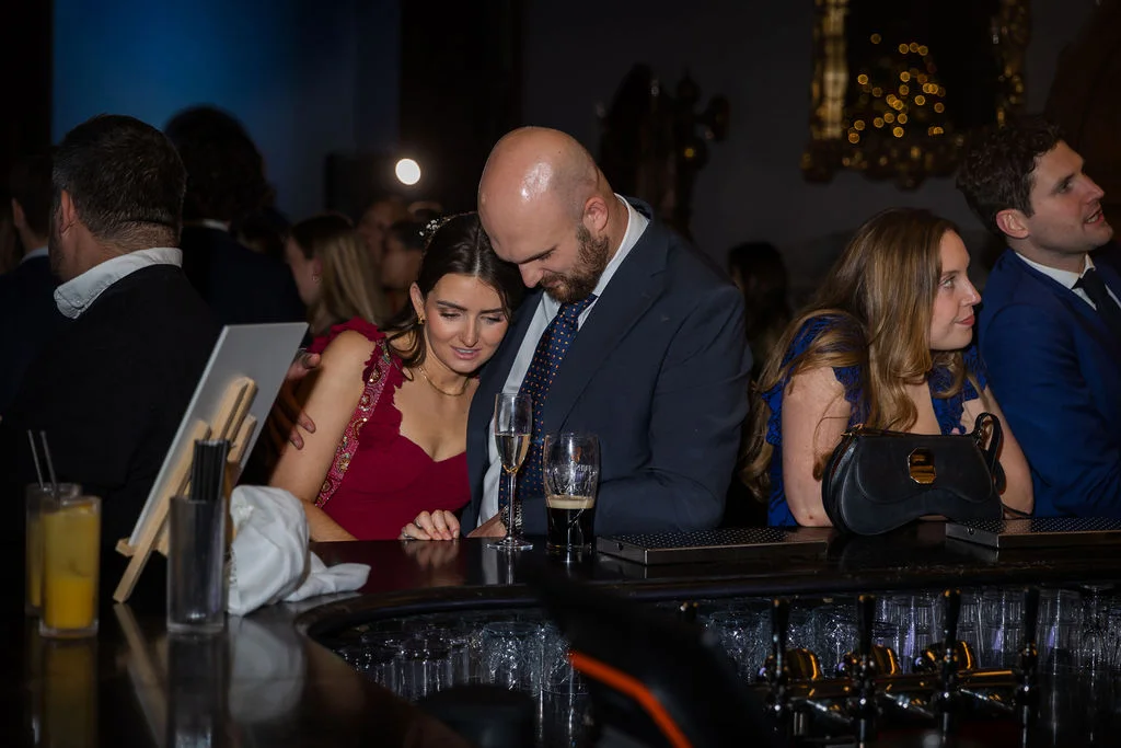 Guests relaxing together at a lively evening drinks reception by a busy bar.