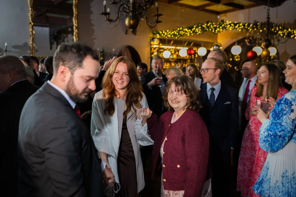 Wedding guests mingle and smile happily in a warmly lit venue interior decorated with fairy lights and chandeliers during the evening reception.