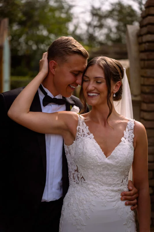 A bride and groom embracing in front of a brick wall.