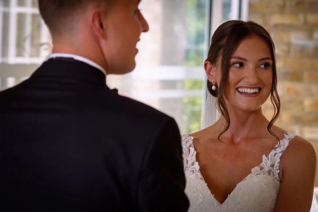 A bride and groom smile at each other during their wedding ceremony.