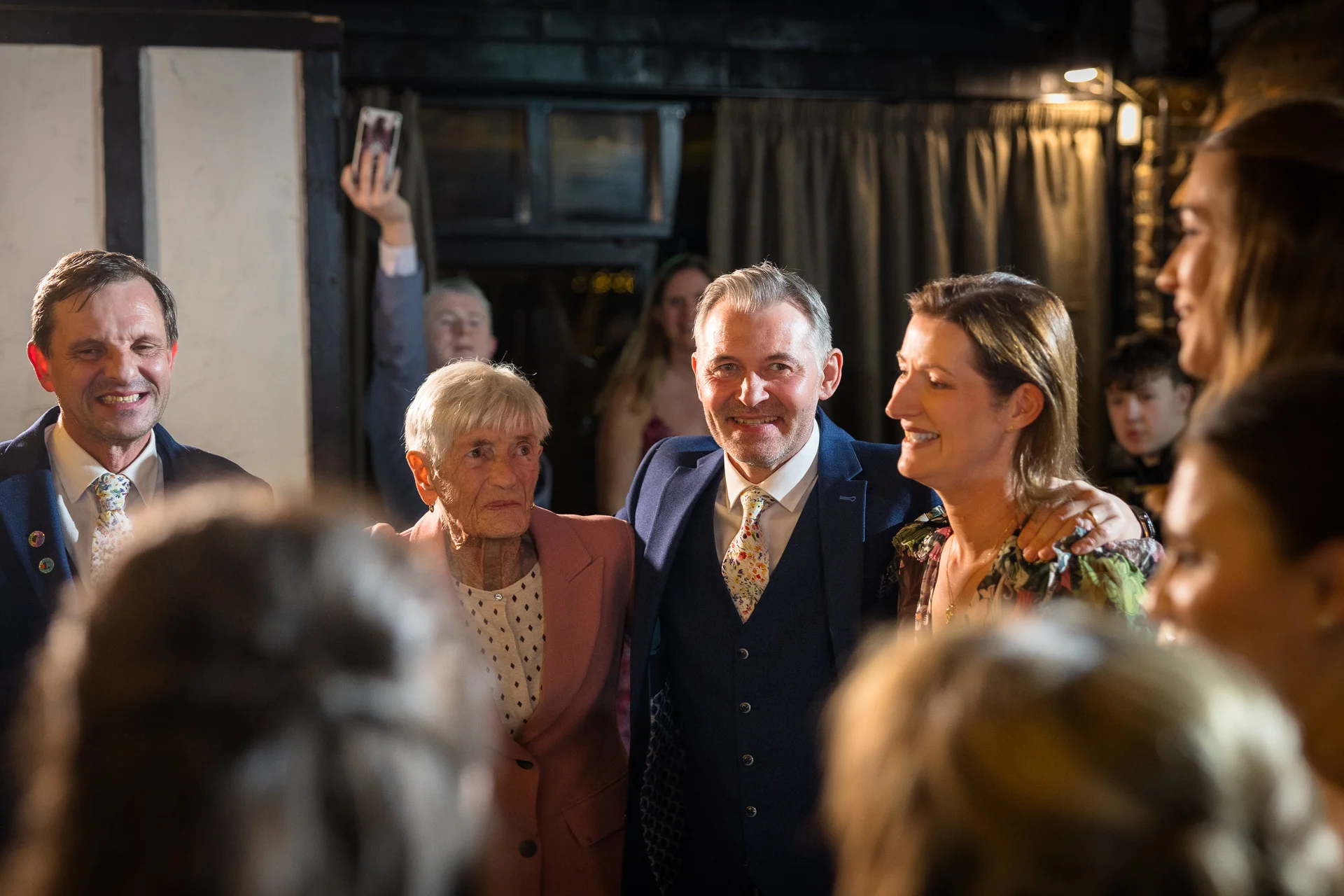Smiling wedding guests and family members gather together indoors during a candid evening reception.