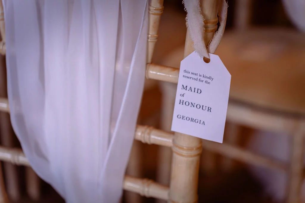 A close up view of a reserved seat tag for the maid of honour hanging from a wooden chair draped with white fabric.