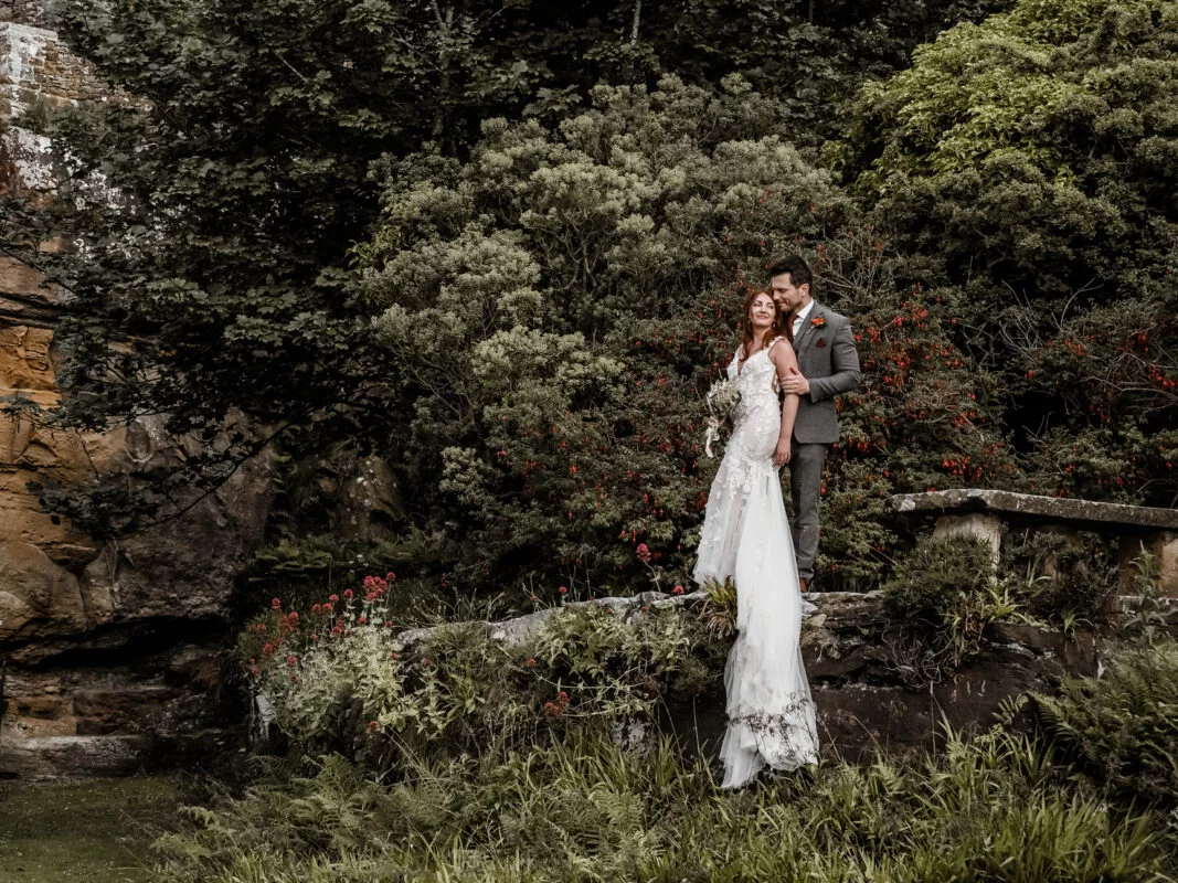 A bride and groom standing on a rock in the garden.