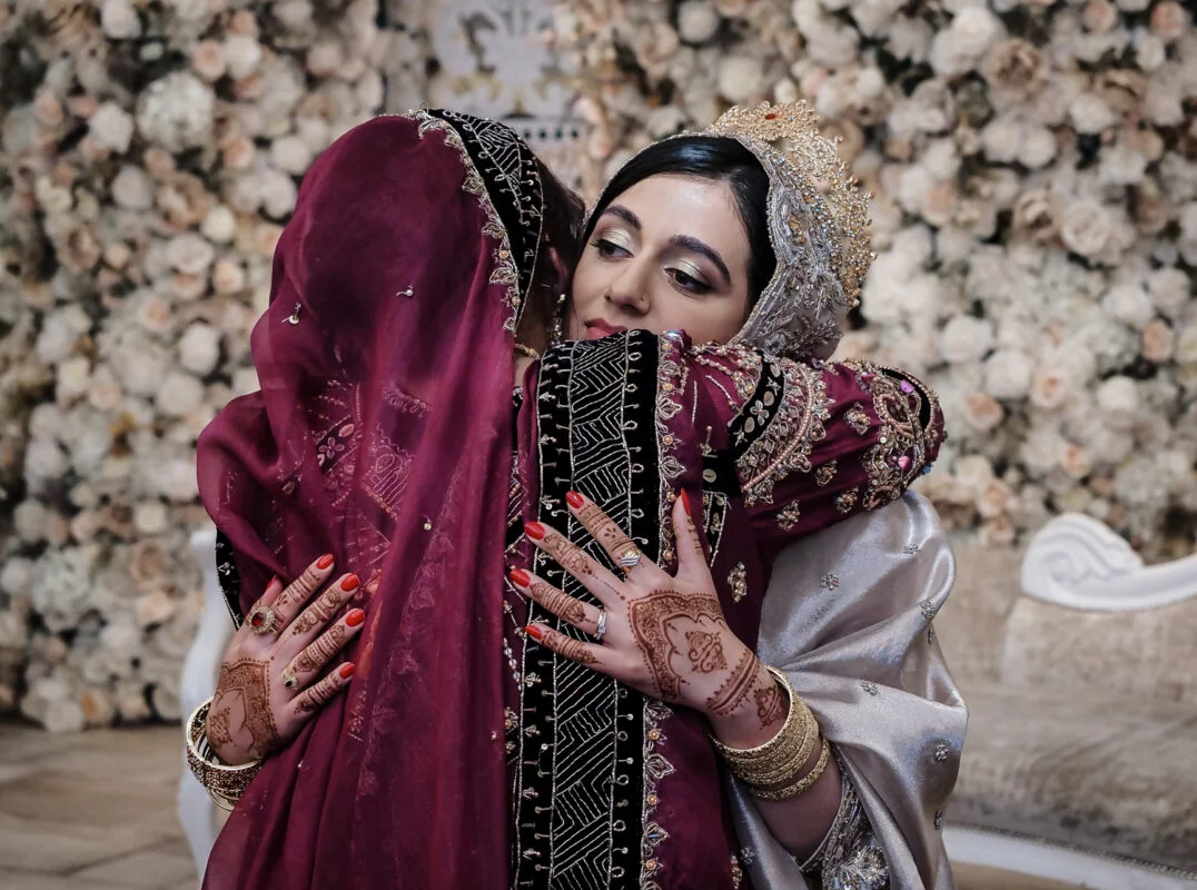 Two women hugging each other in front of a floral backdrop.