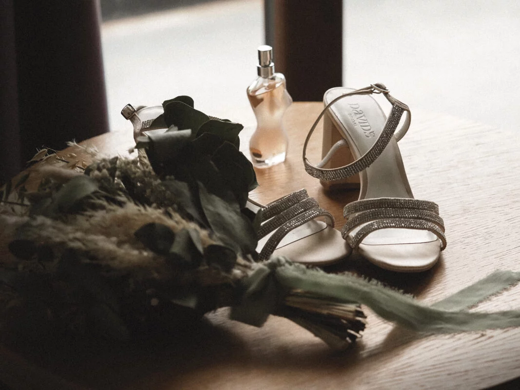 Wedding shoes and bouquet on a table next to a window.
