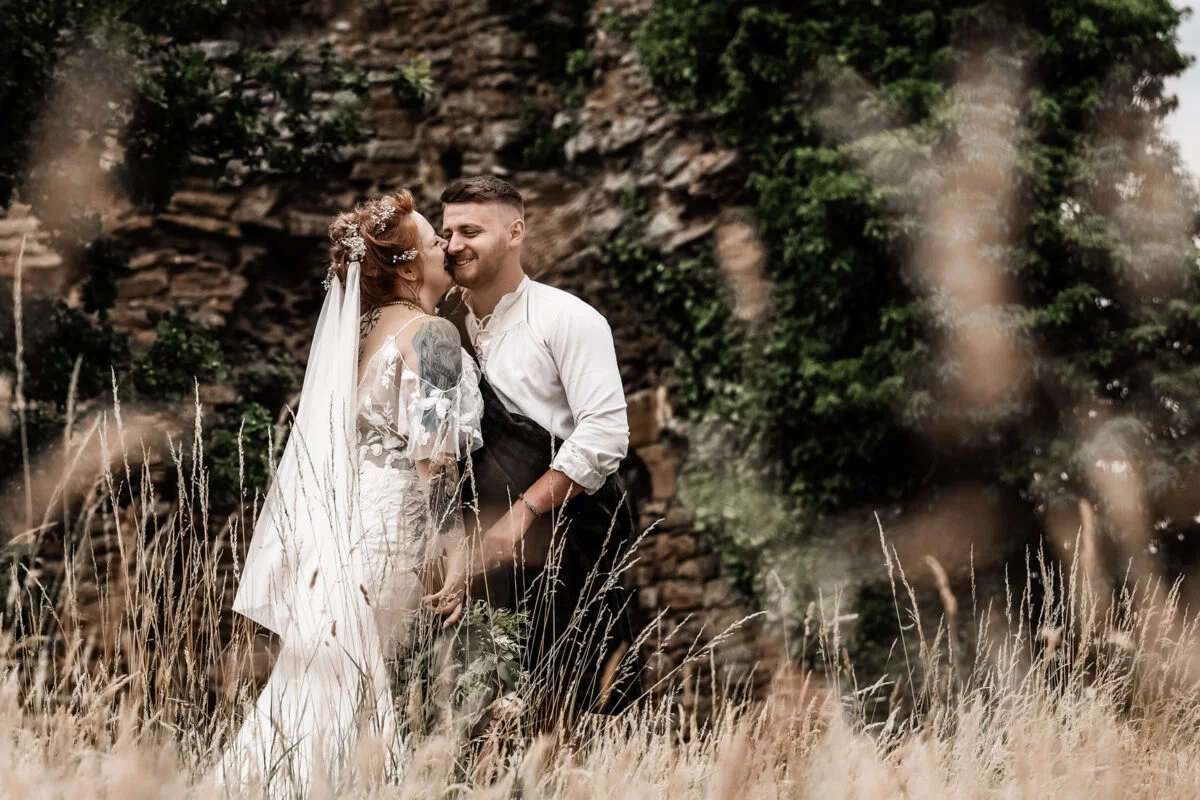 A bride and groom standing in tall grass with a castle in the background.