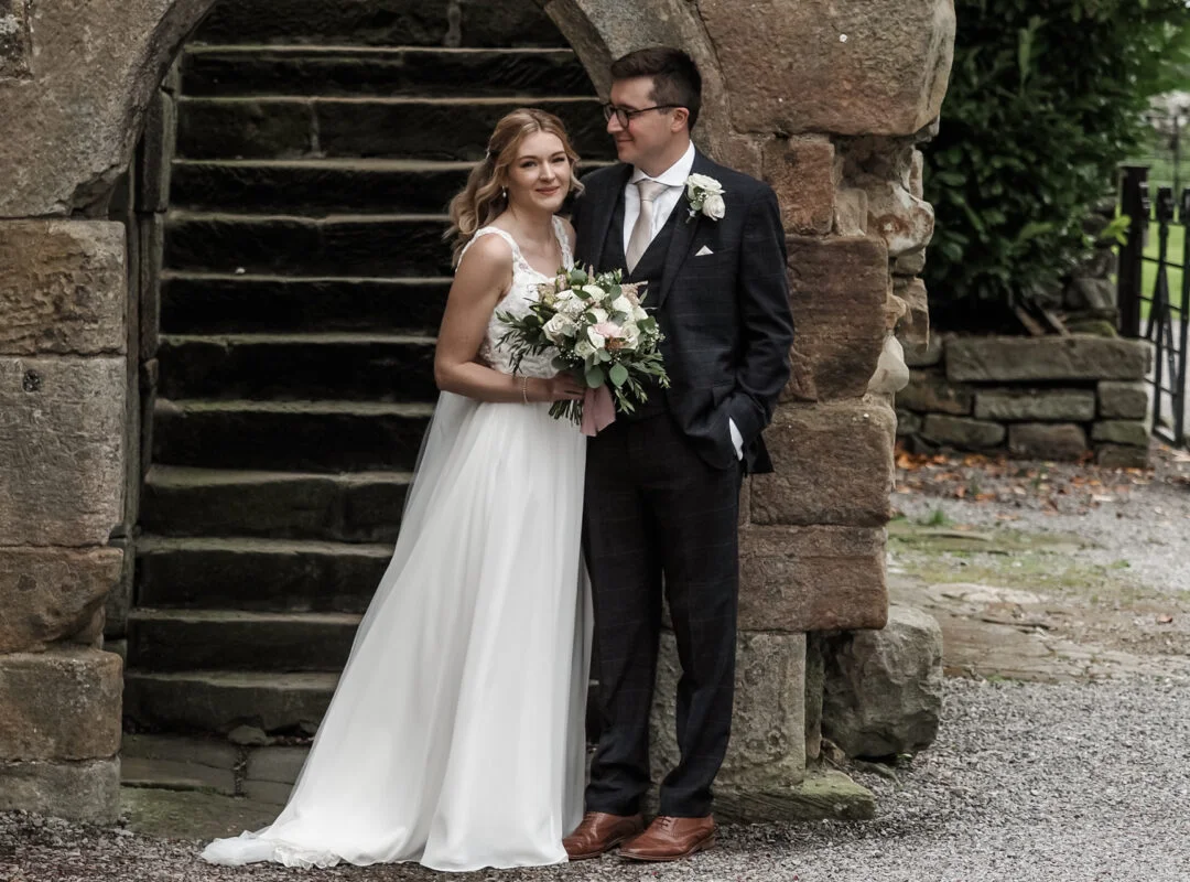 A bride and groom standing in front of a stone archway.