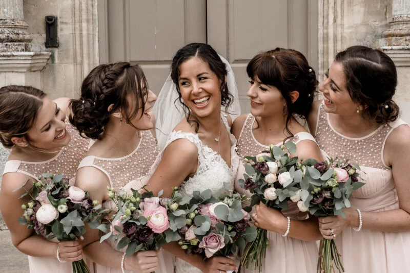 A bride and her bridesmaids laughing in front of a building.