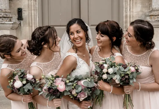 A bride and her bridesmaids laughing in front of a building.