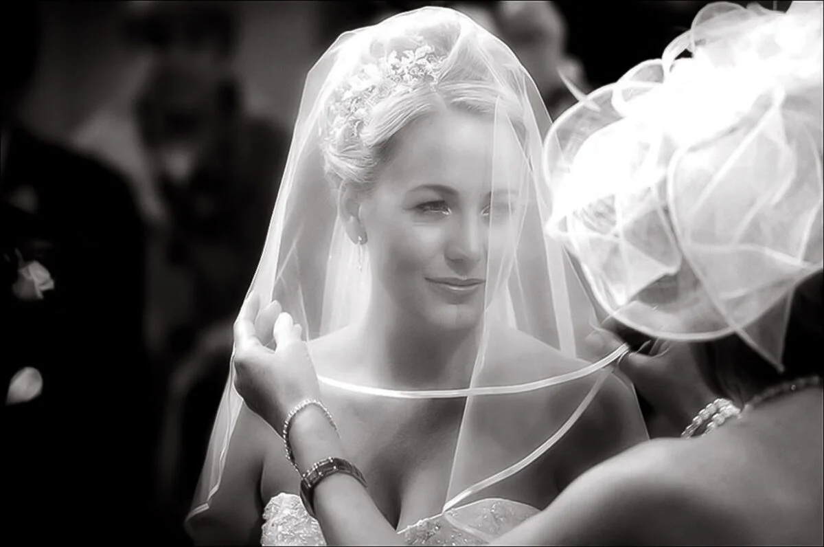 Black and white photo of a bride putting on her veil.