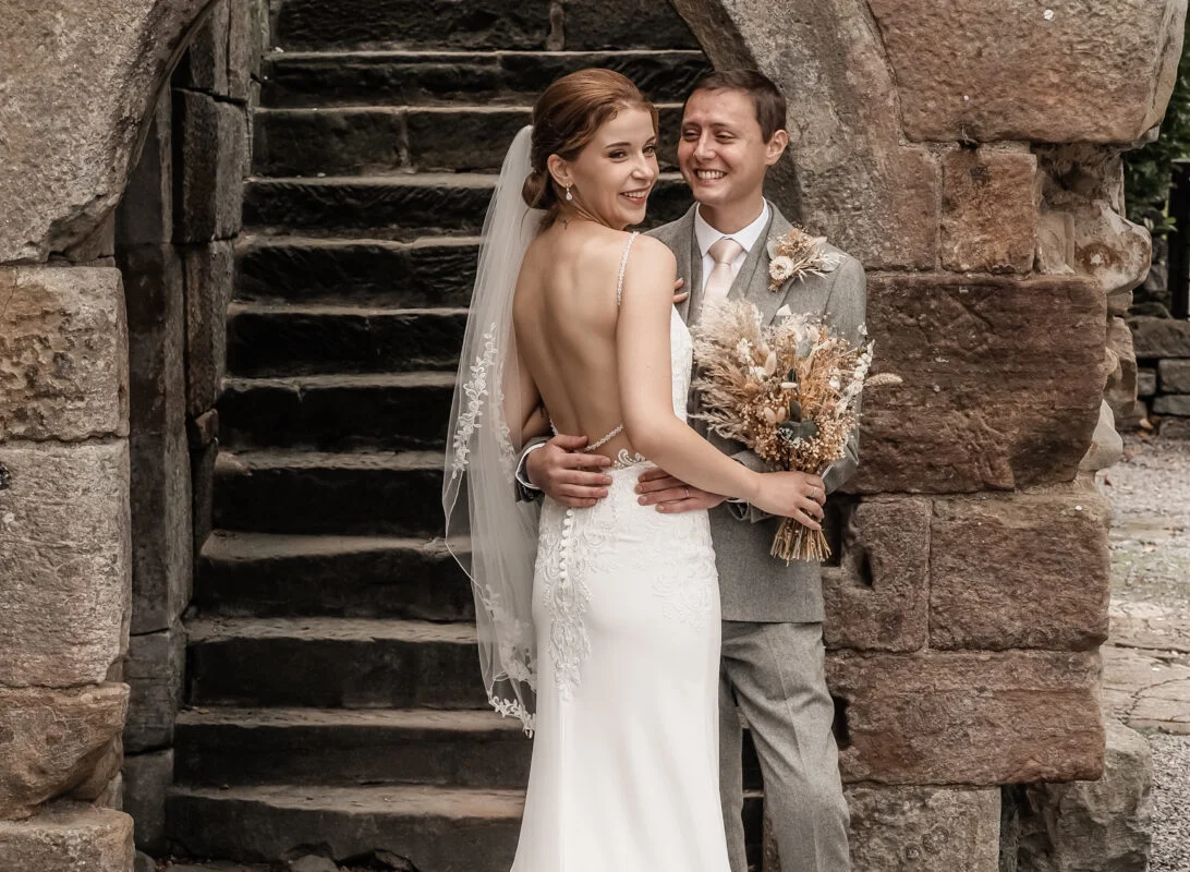 A bride and groom posing in front of a stone archway.