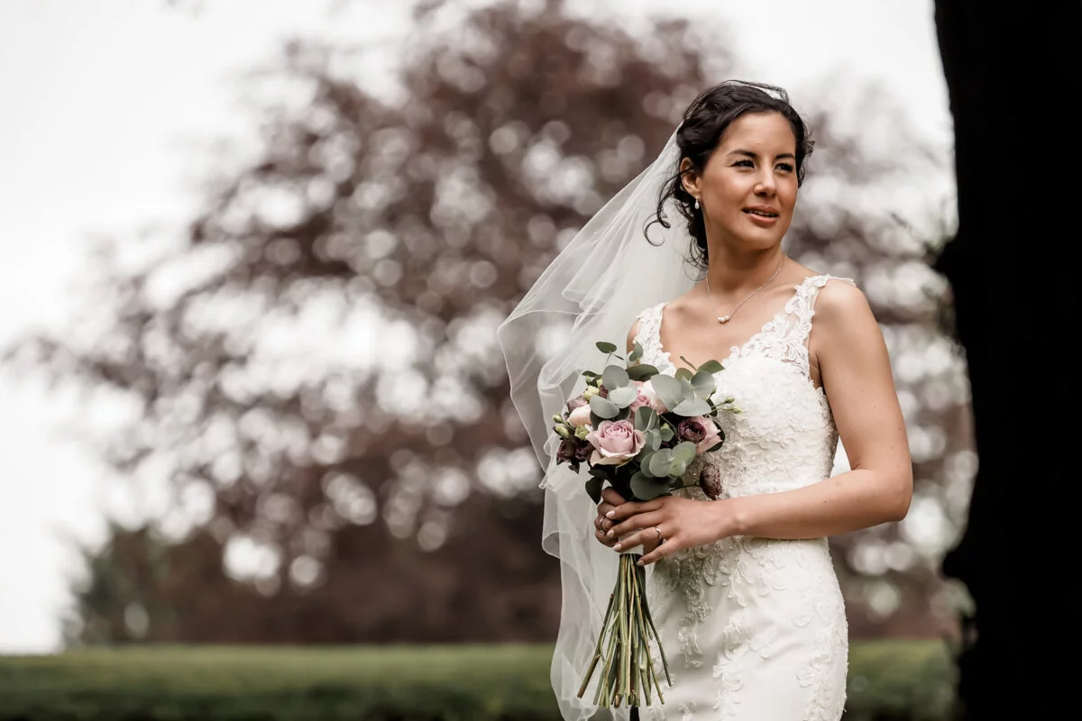 A bride holding her bouquet in front of a tree.