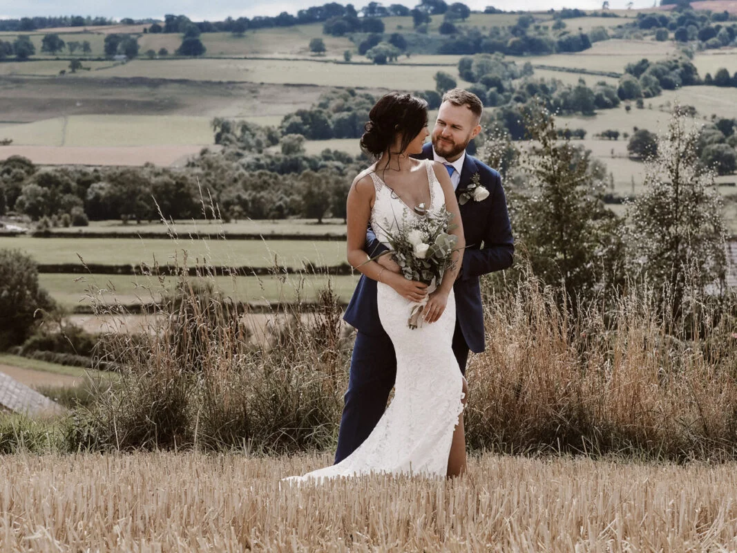 A bride and groom embracing in a field.