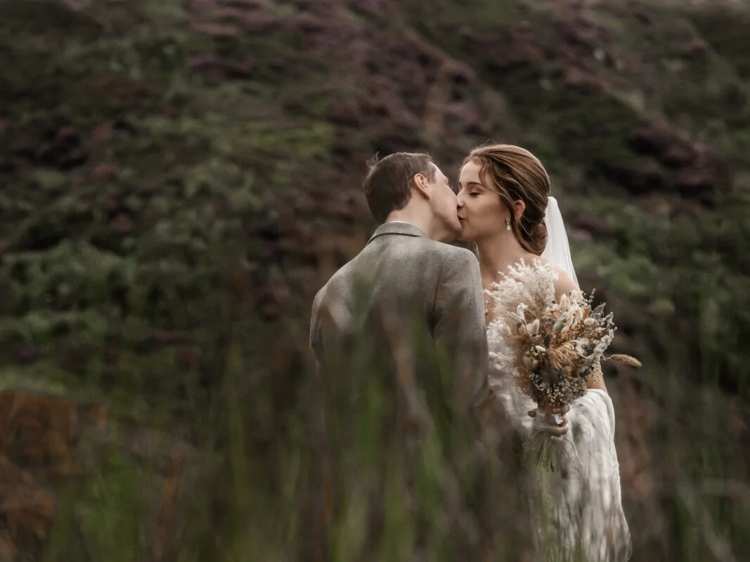 A bride and groom kissing in the grass.