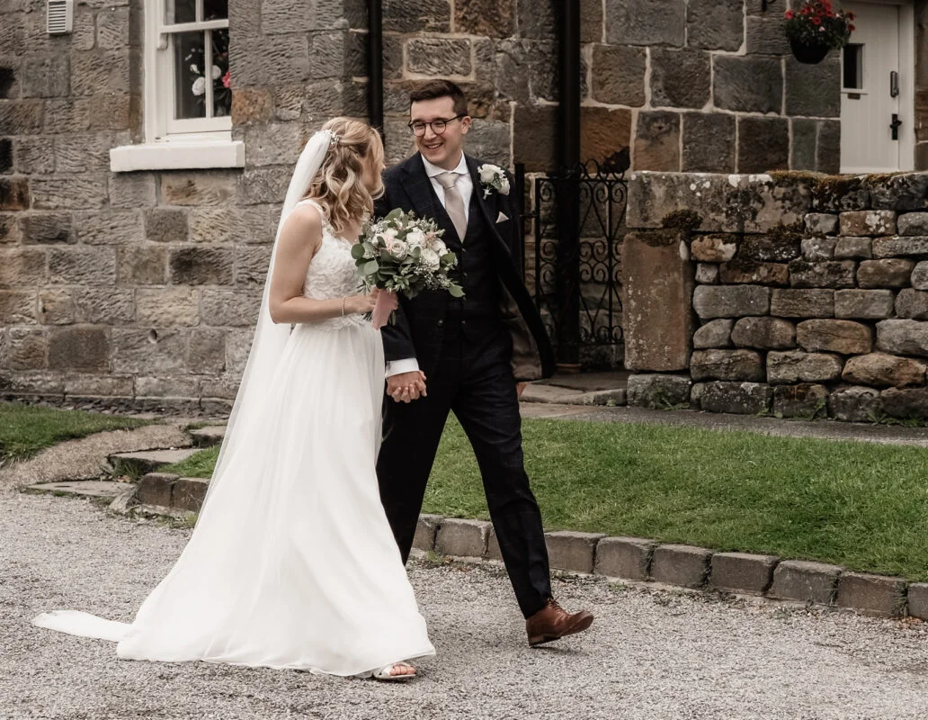 A bride and groom walking in front of a stone building.
