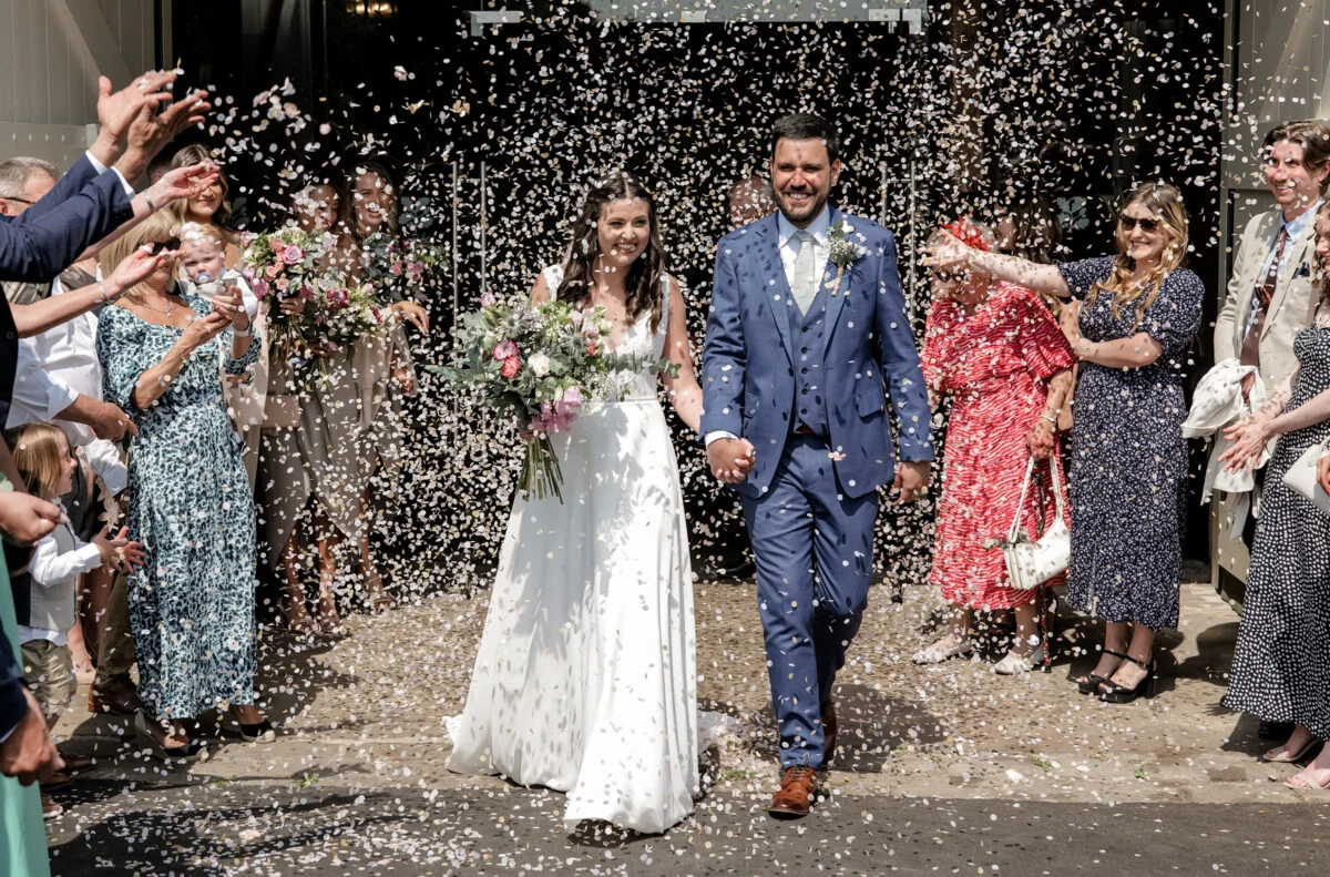 A bride and groom are being confettied at their wedding.