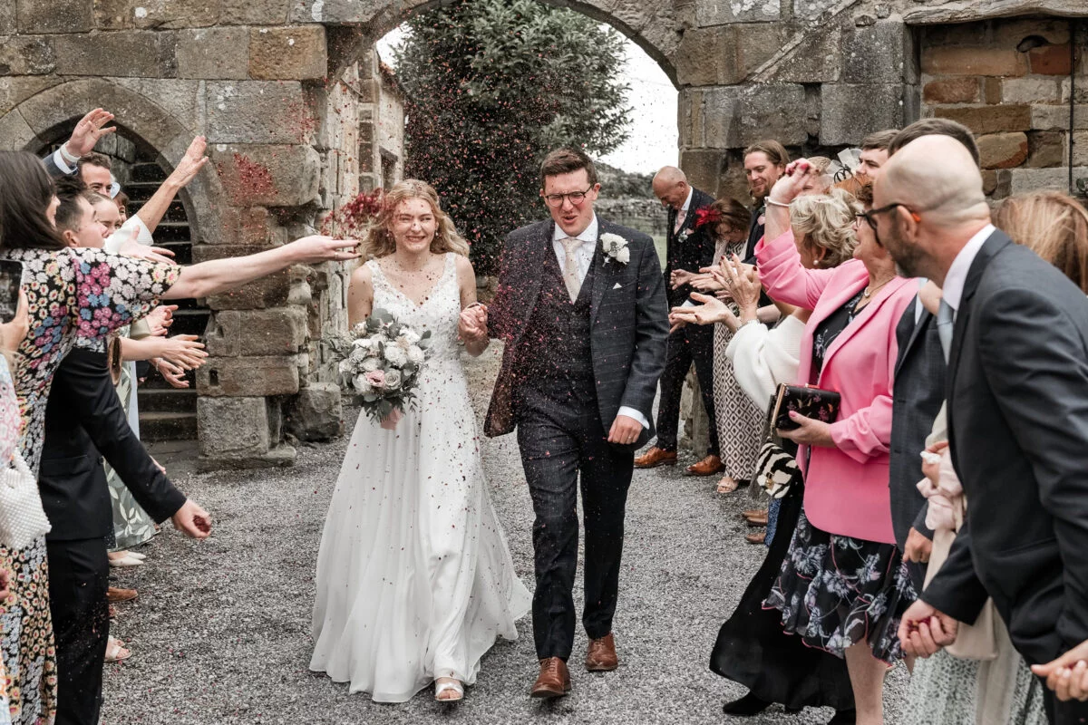 A bride and groom walk out of a castle with confetti thrown at them.