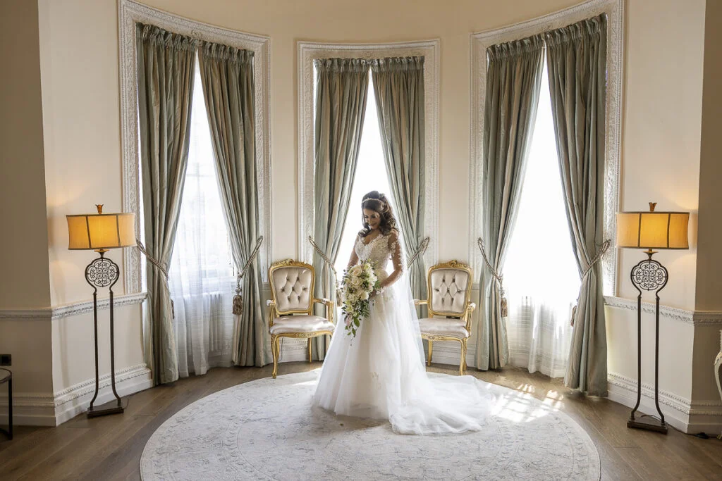 A bride in a wedding dress standing in a room with large windows.