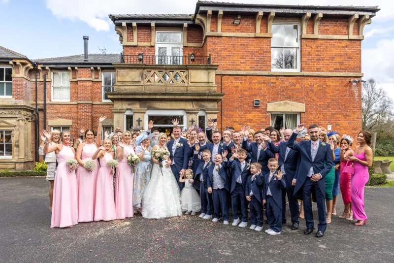 A wedding party posing in front of a large mansion.