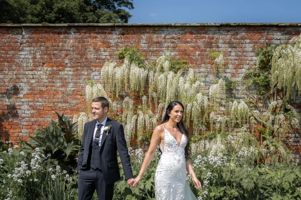 A bride and groom walking in front of a brick wall.