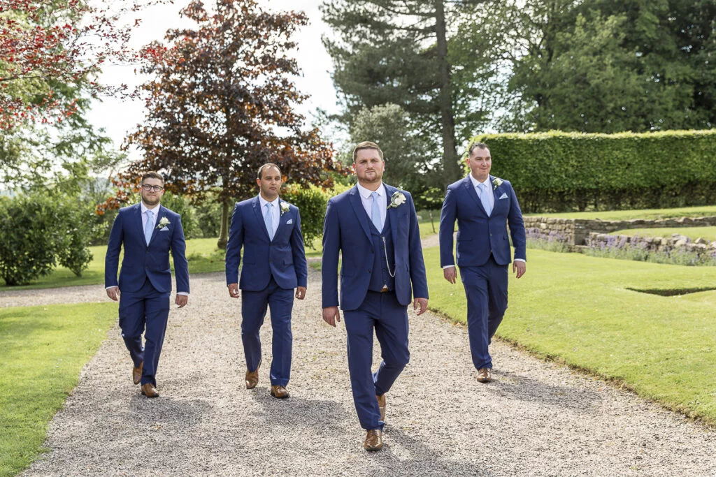 A group of groomsmen walking down a path in a garden.