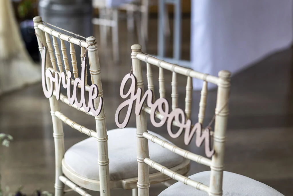 Two wooden chairs with the words bride and groom on them.