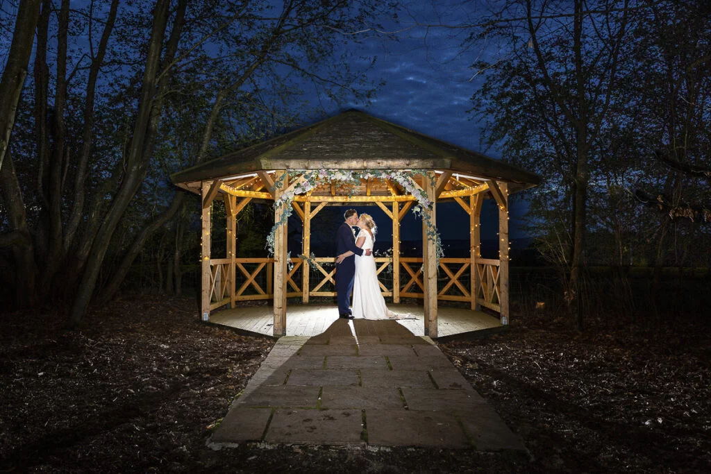 A bride and groom standing in front of a gazebo at night.