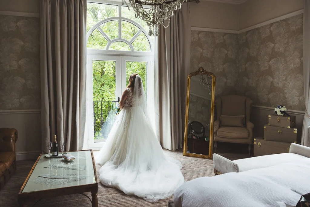 A bride in a wedding dress standing in front of a window.