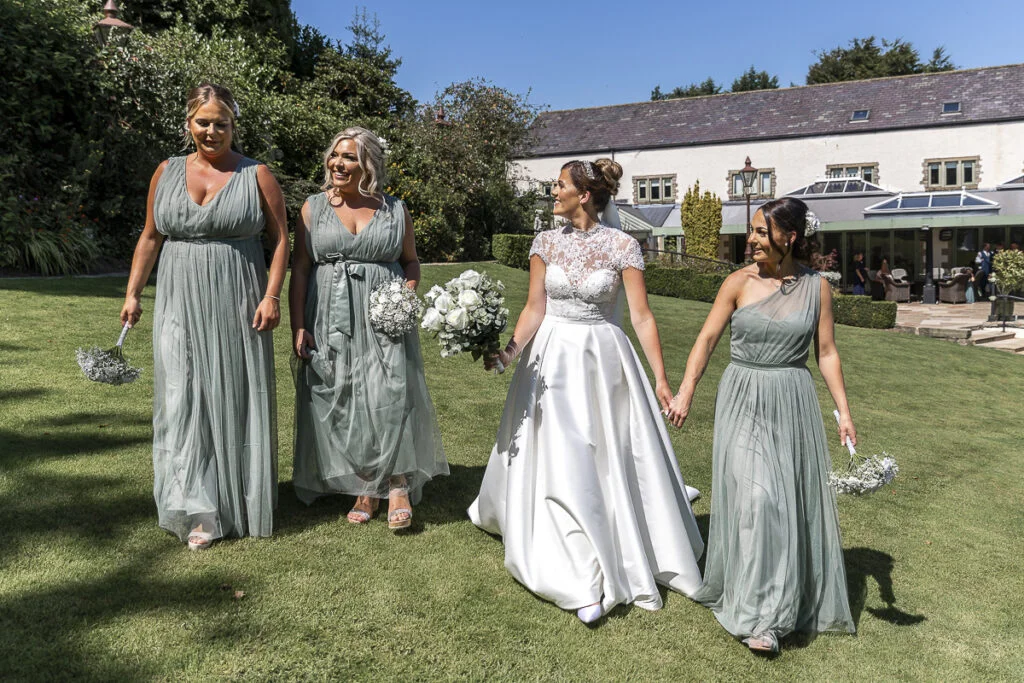 A bride and her bridesmaids walk in front of a house.