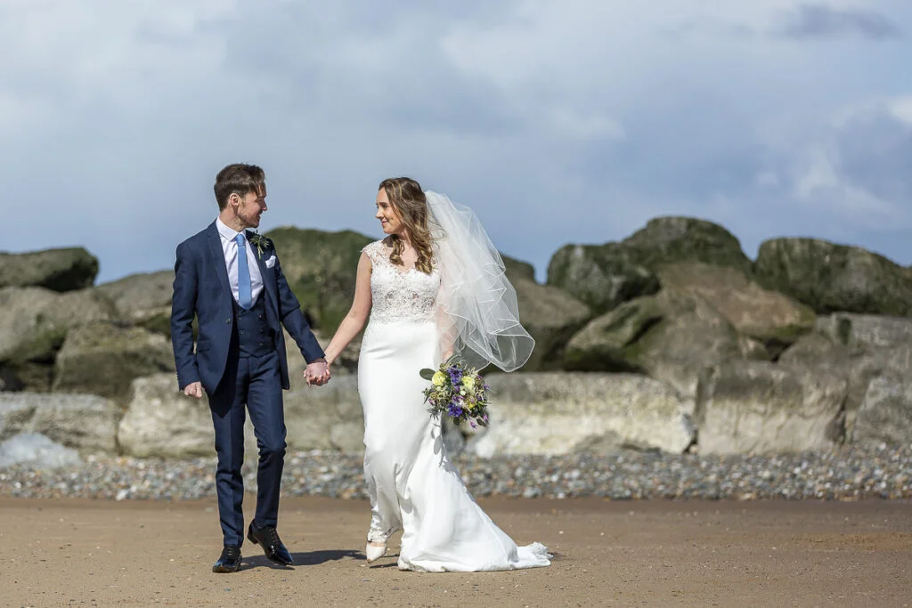 A bride and groom walking on the beach.