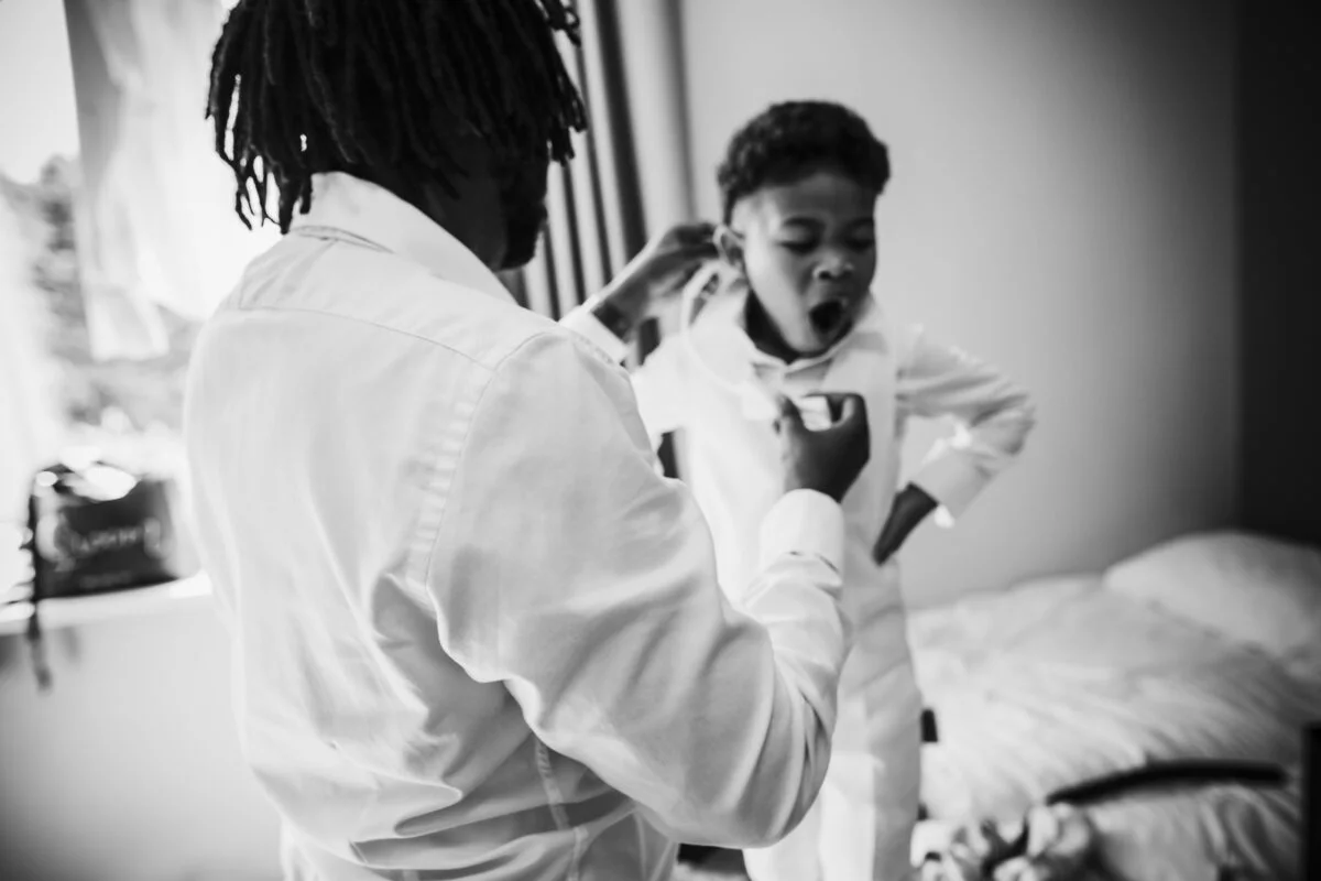 A black and white photo of a man putting on a tuxedo.