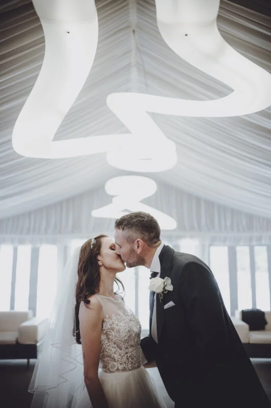 A bride and groom kissing in a tent.