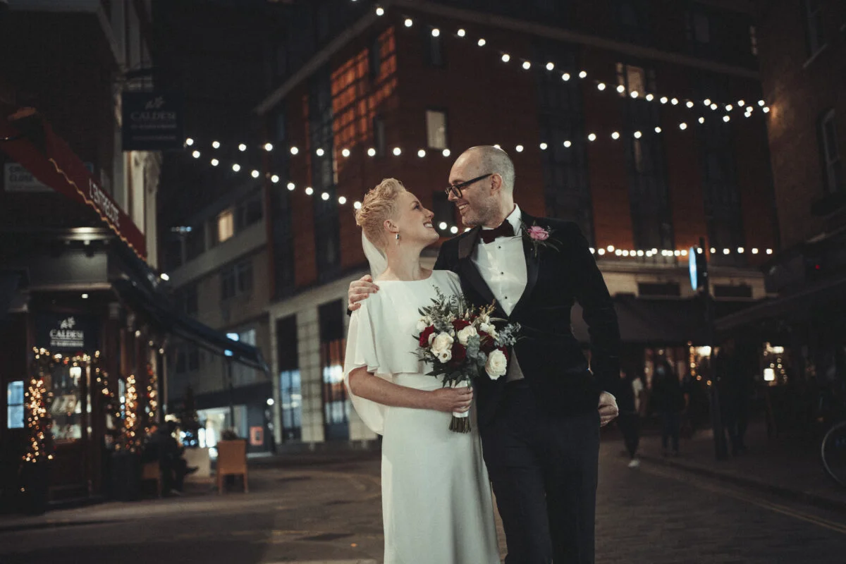 A bride and groom standing in a city street at night.