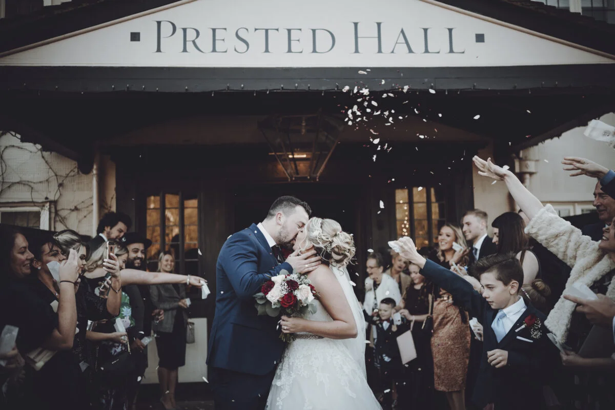 A bride and groom kissing in front of the prested hall.