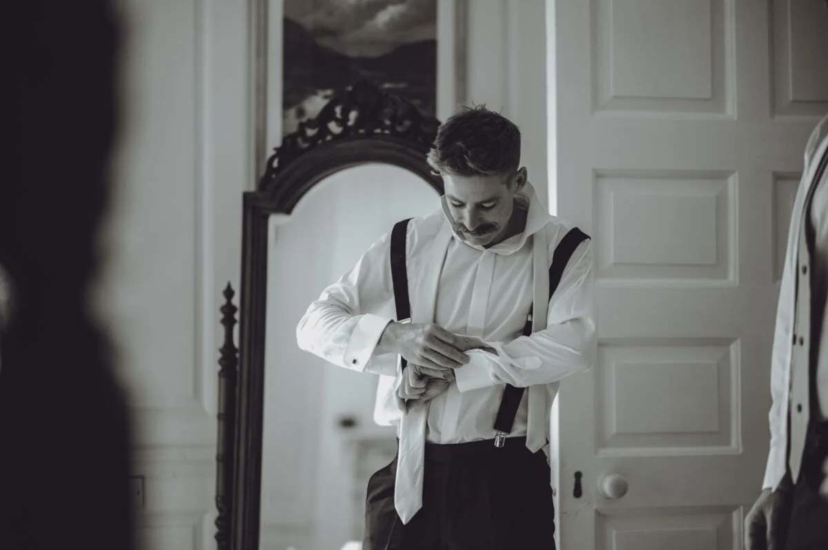 A man is adjusting his tie in front of a mirror.