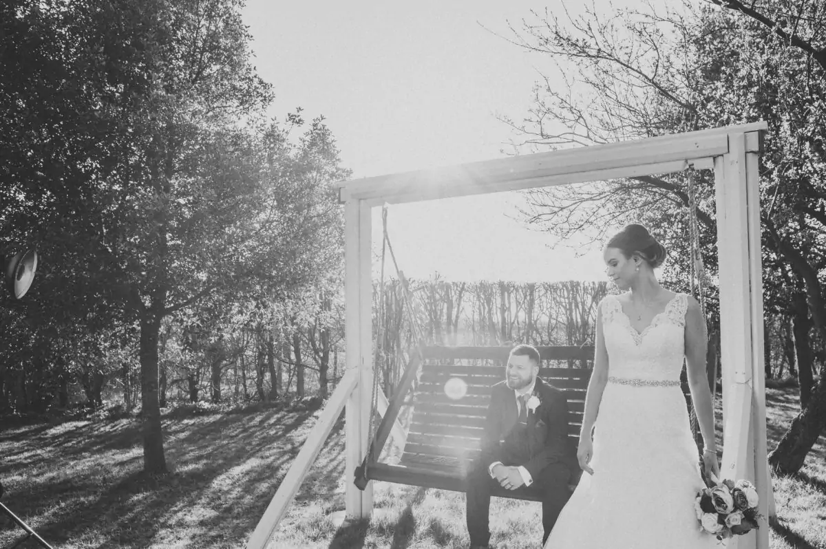 A black and white photo of a bride and groom on a swing.