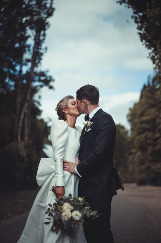 A bride and groom kissing in the woods.