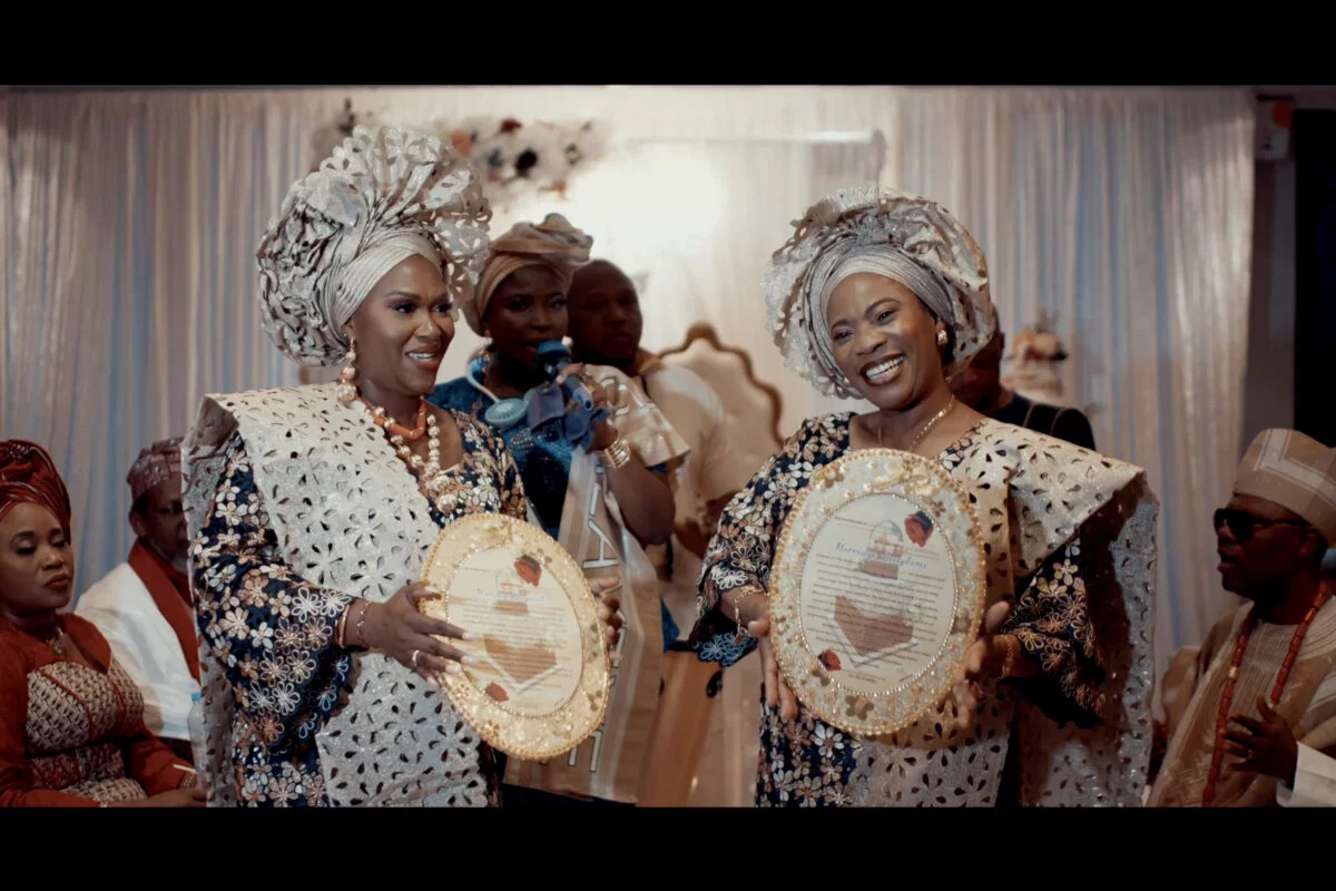 Two women in traditional attire are holding plates in front of each other.