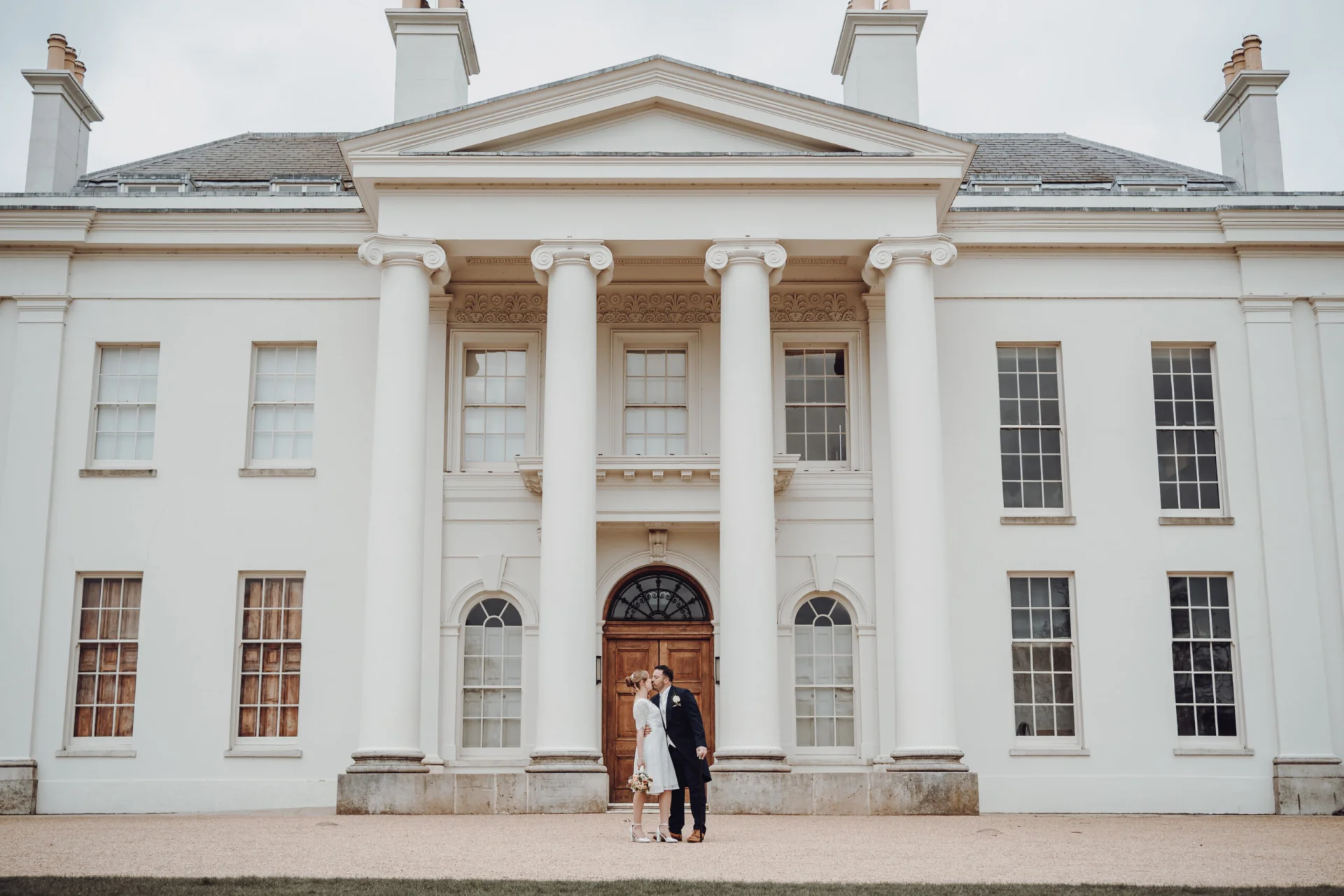 A bride and groom standing in front of a white mansion. (listing)