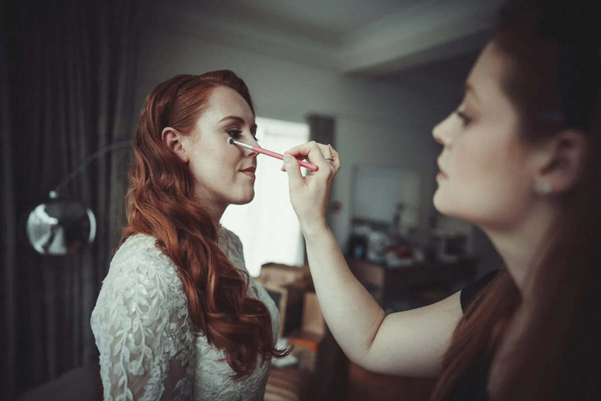 A bride getting her makeup done by a wedding photographer.