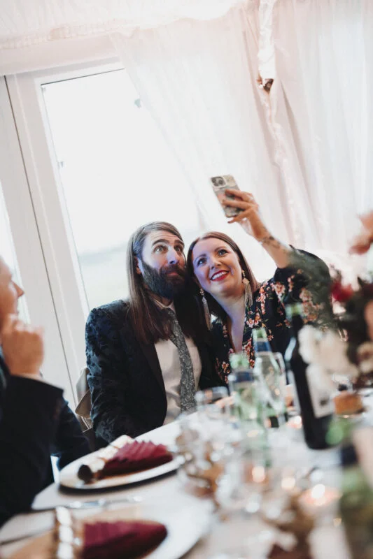A man and woman taking a selfie at a table.