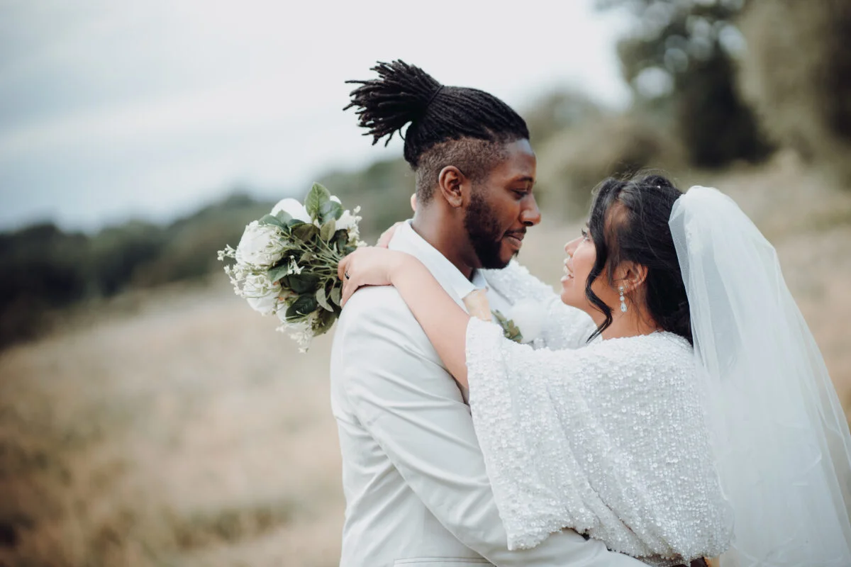 A bride and groom hugging in a field.