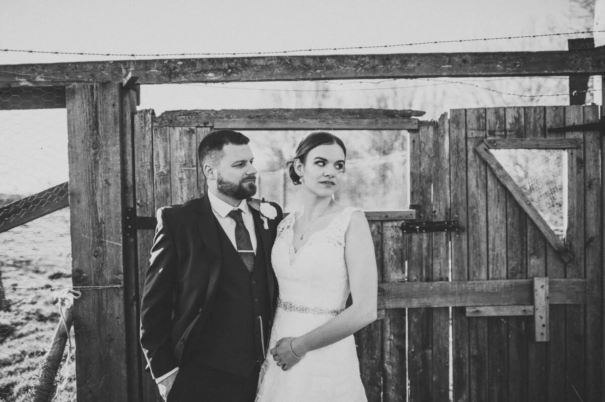 A bride and groom standing in front of a wooden gate.