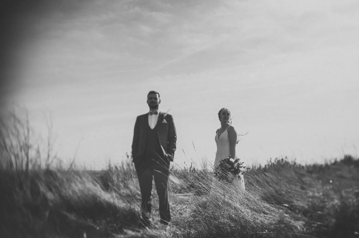 A bride and groom standing in a field of tall grass.
