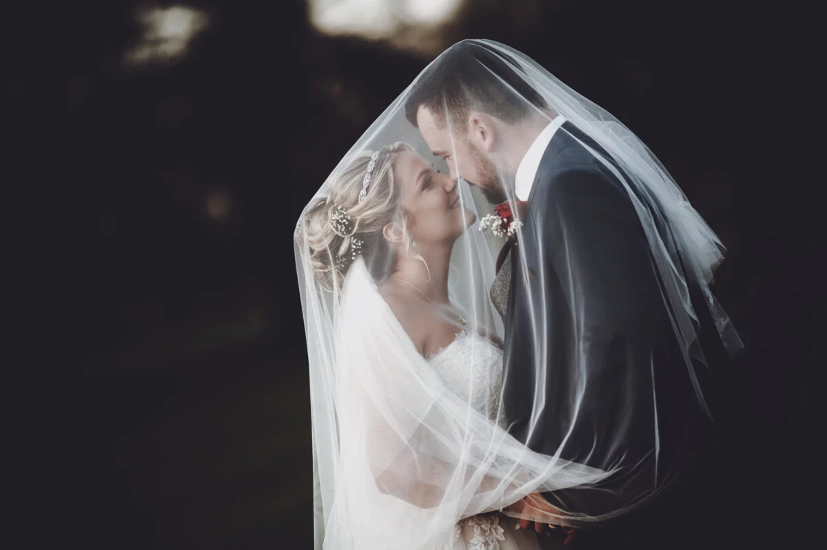 A bride and groom kissing under a veil.