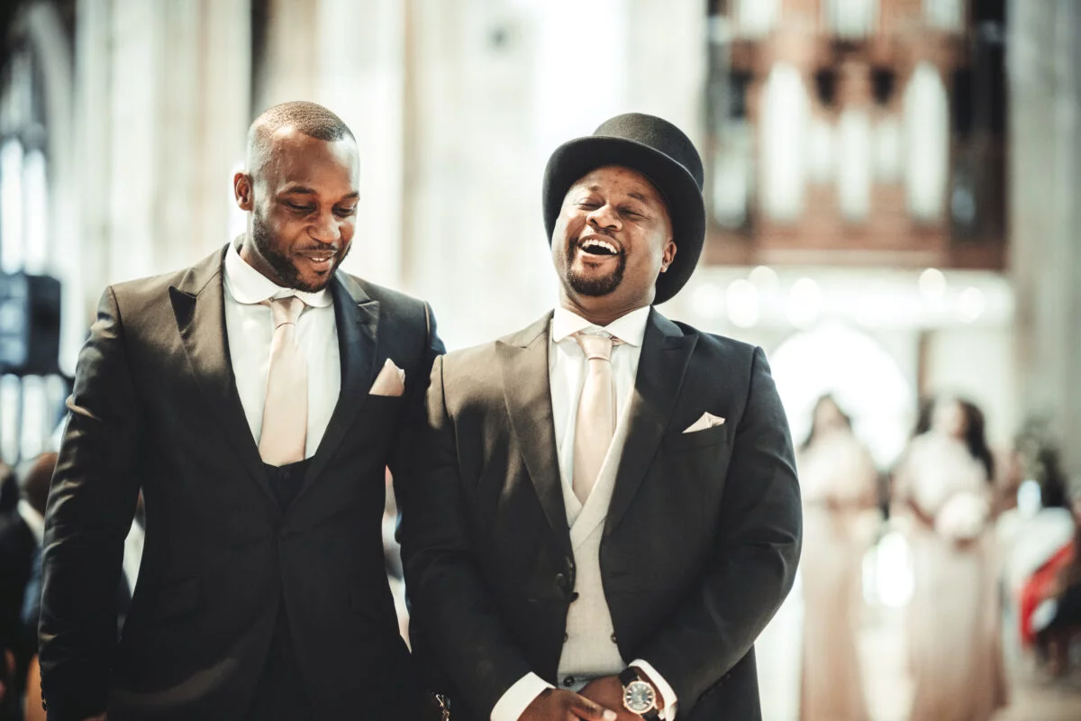 Two men in tuxedos laughing in a church.