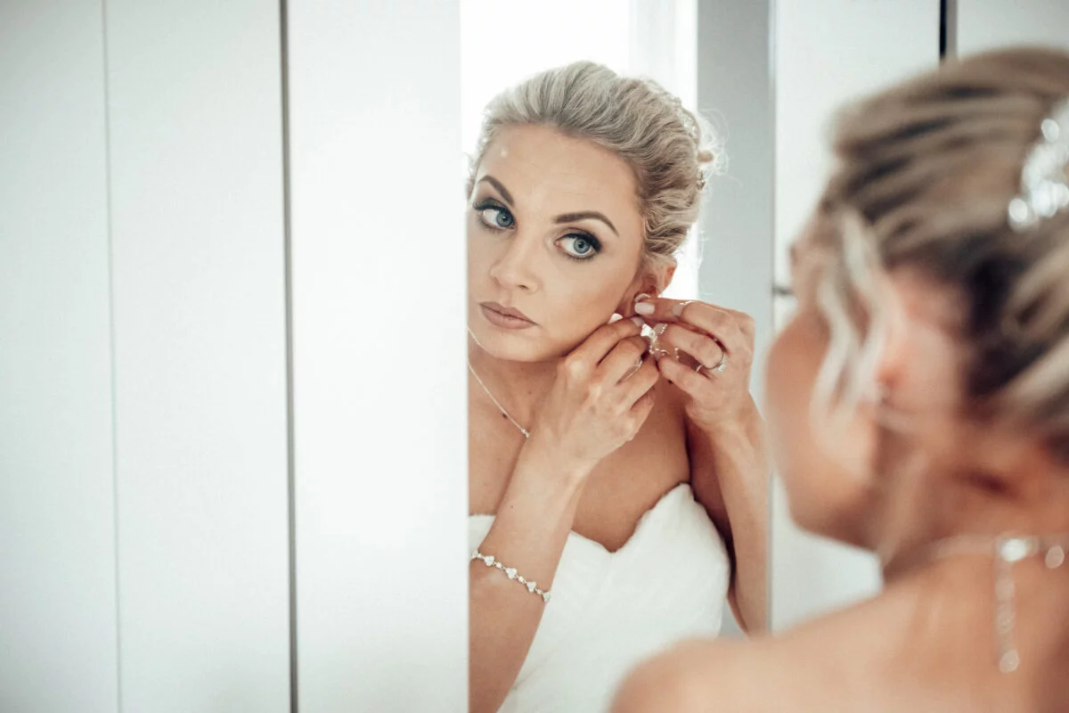 A bride putting on her wedding earring in front of a mirror.