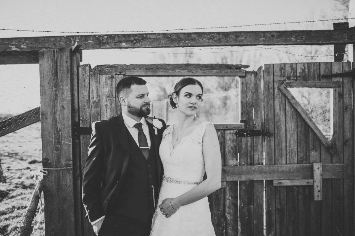 A bride and groom standing in front of a wooden gate.