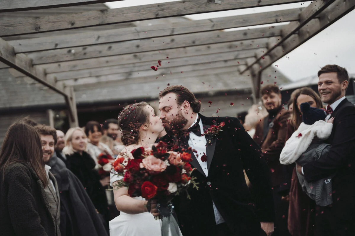 A bride and groom kissing under a pergola.